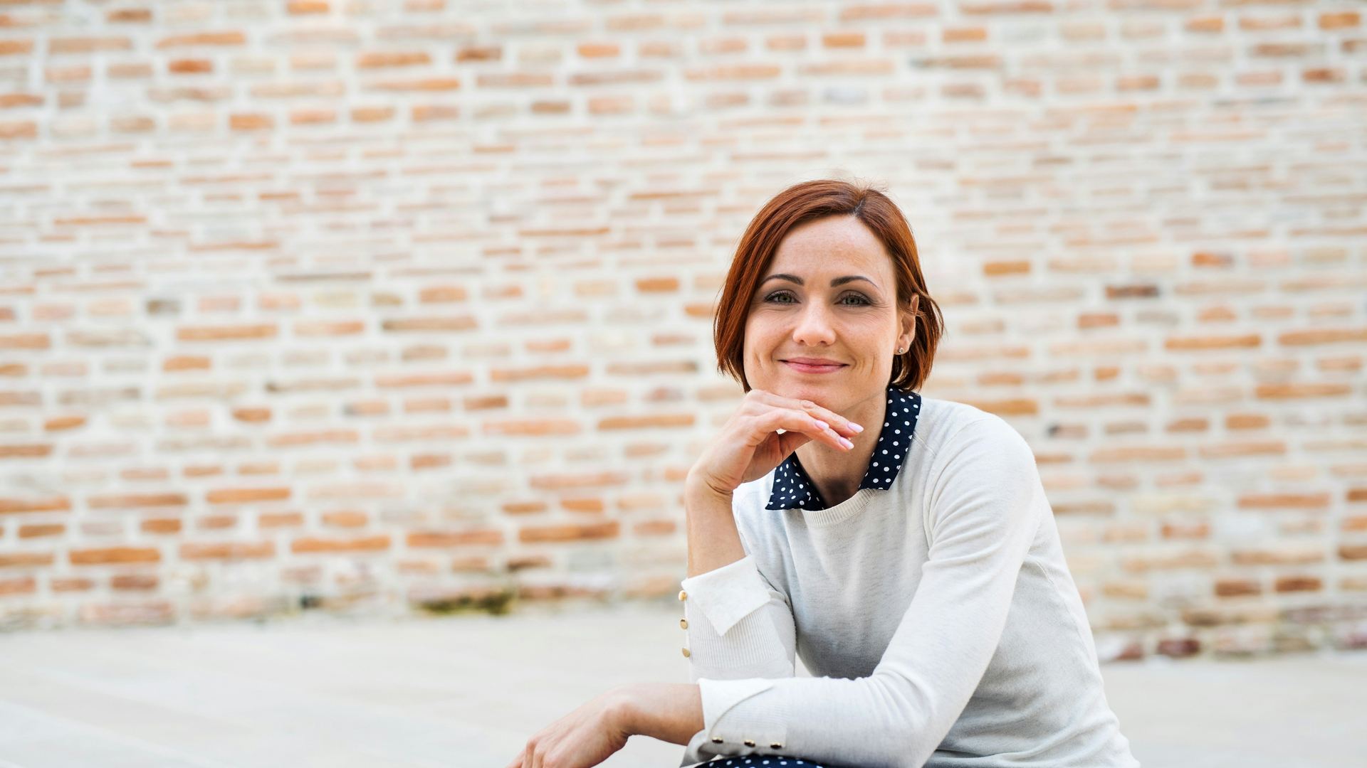 Managerka siedzi przed jasną ceglaną ścianą