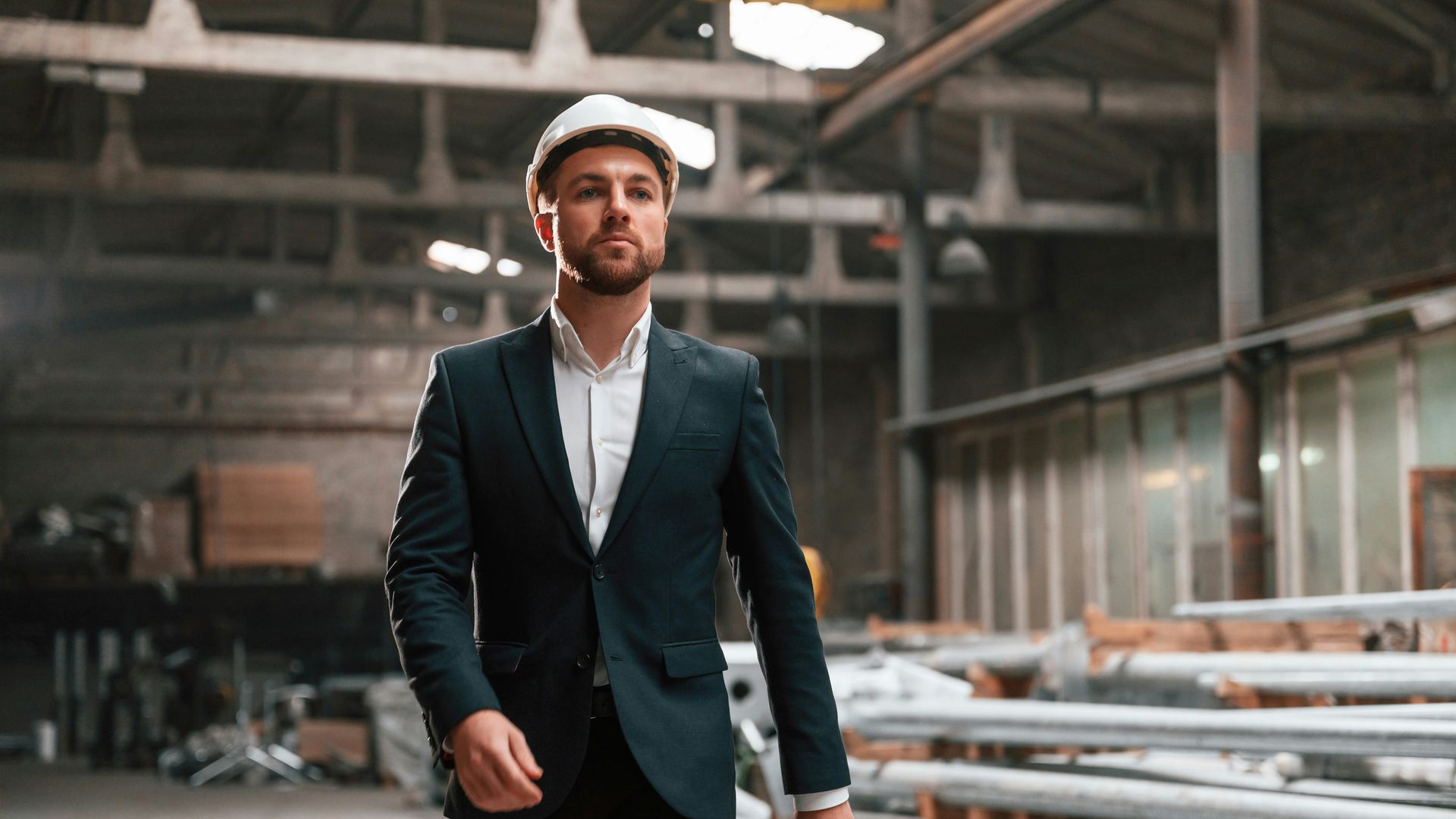 Manager w garniturze i kasku idzie przez halę produkcyjną